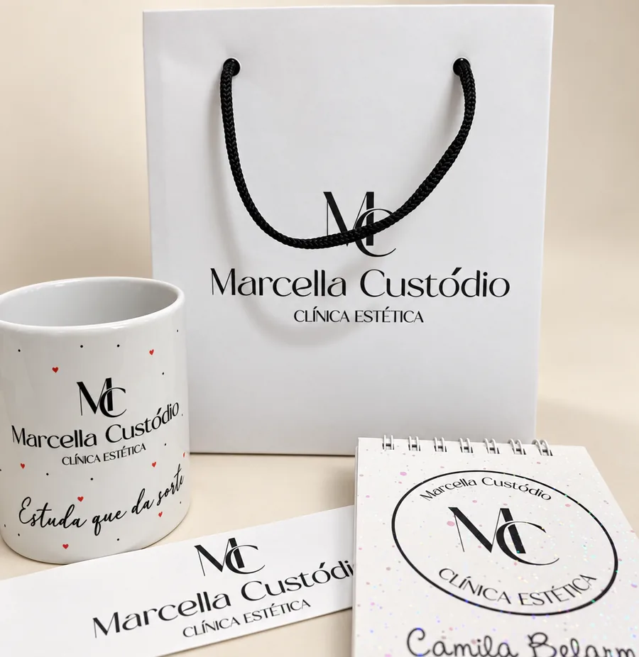 Kit personalizado da Marcella Custódio Clínica Estética: sacola branca, caneca, bloco de anotações espiral e cartão, todos com a mesma logo.